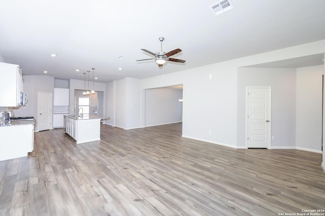 unfurnished living room with visible vents, a ceiling fan, a sink, light wood finished floors, and baseboards