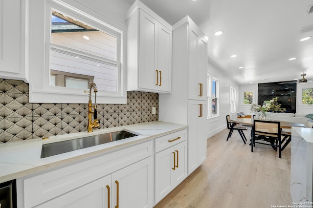 kitchen featuring tasteful backsplash, light wood finished floors, light stone counters, white cabinets, and a sink