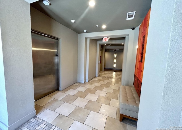 hall featuring light tile patterned flooring, visible vents, and baseboards