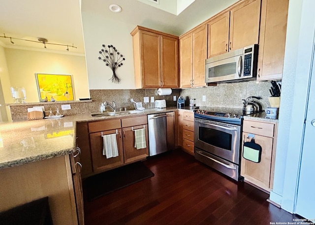 kitchen featuring light stone counters, a peninsula, a sink, decorative backsplash, and stainless steel appliances