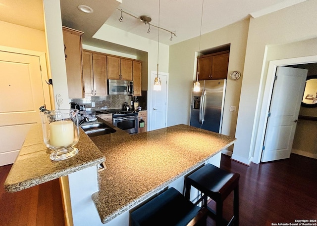 kitchen with a sink, stainless steel appliances, a peninsula, brown cabinetry, and decorative backsplash