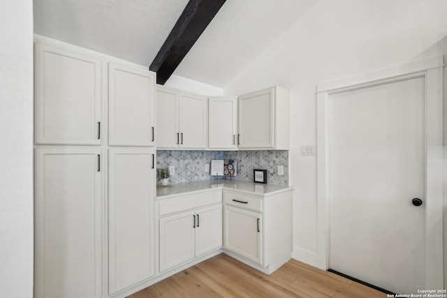 kitchen featuring light wood-type flooring, vaulted ceiling with beams, light countertops, white cabinetry, and tasteful backsplash