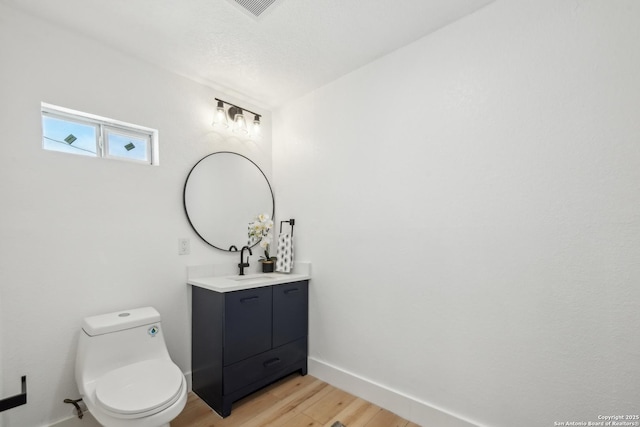 half bathroom with vanity, toilet, wood finished floors, and baseboards