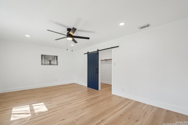 spare room with recessed lighting, a barn door, light wood finished floors, baseboards, and ceiling fan