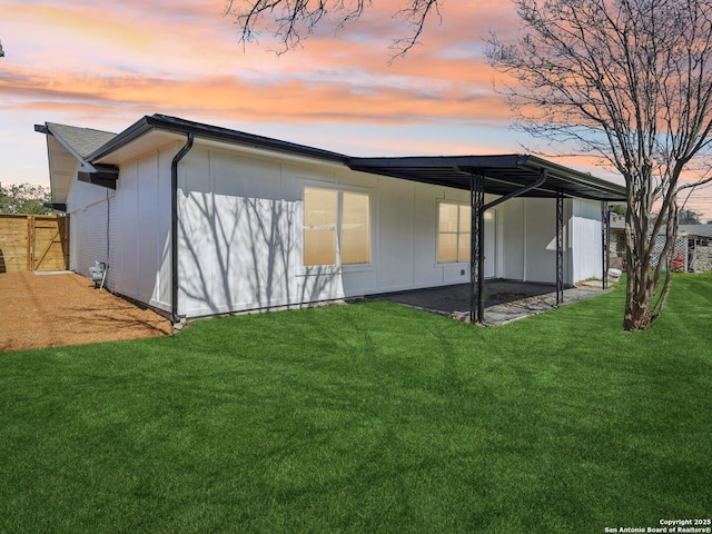 back of house at dusk with a patio, a yard, and fence