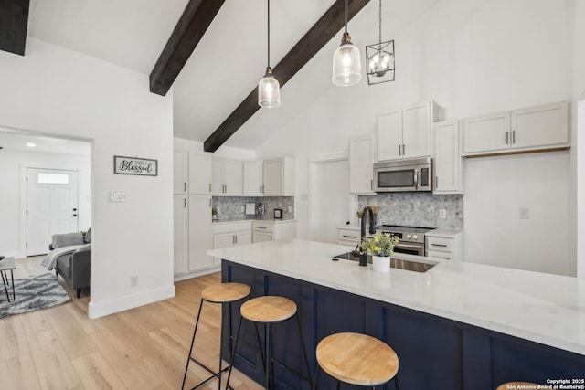 kitchen featuring a kitchen bar, a sink, tasteful backsplash, white cabinetry, and stainless steel appliances