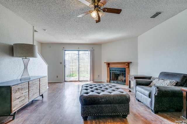 living room featuring visible vents, a ceiling fan, a textured ceiling, wood finished floors, and a fireplace