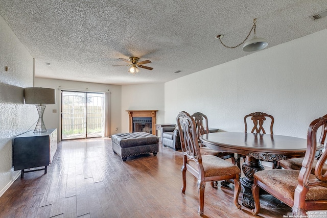 dining area with visible vents, wood finished floors, ceiling fan, and a textured wall