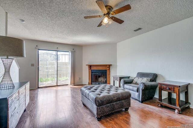 living area featuring visible vents, a fireplace, ceiling fan, hardwood / wood-style flooring, and a textured ceiling