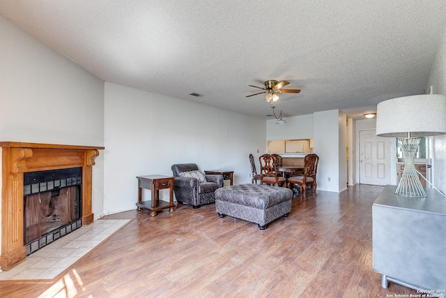 living room with a tile fireplace, a textured ceiling, a ceiling fan, and wood finished floors