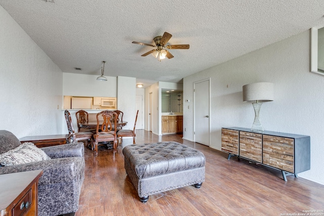 living room with wood finished floors, a ceiling fan, a textured wall, and a textured ceiling