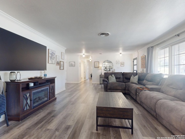 living room featuring baseboards, wood finished floors, visible vents, and ornamental molding