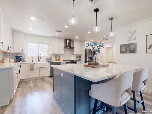 kitchen with a kitchen island, appliances with stainless steel finishes, white cabinetry, wall chimney exhaust hood, and backsplash