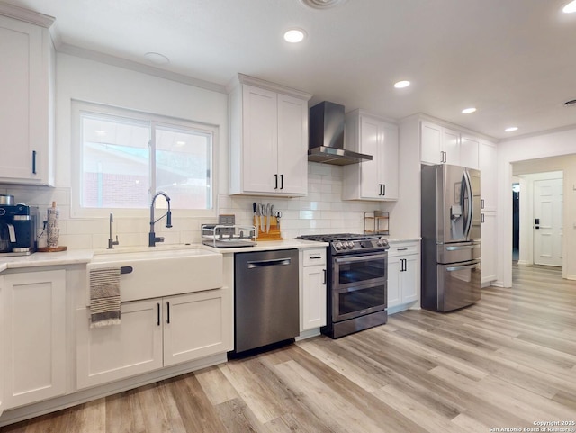 kitchen featuring a sink, light wood-style floors, appliances with stainless steel finishes, and wall chimney range hood