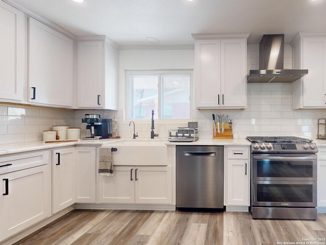 kitchen with light countertops, wall chimney range hood, light wood-style floors, and stainless steel appliances