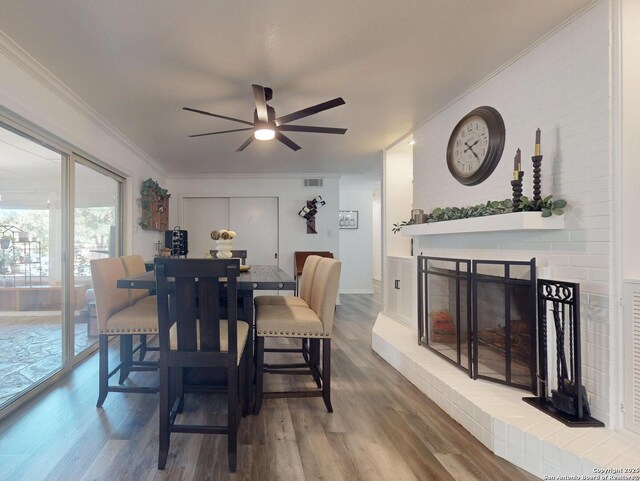 dining area featuring visible vents, a brick fireplace, crown molding, ceiling fan, and wood finished floors