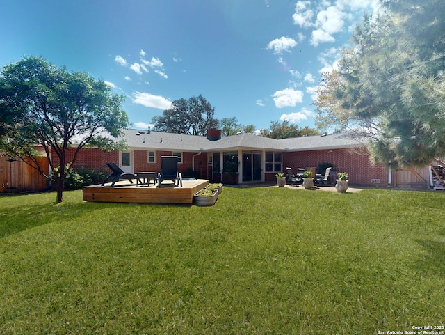 rear view of property featuring brick siding, a lawn, a deck, and fence