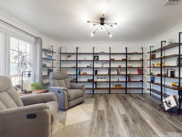 living area with visible vents, wood finished floors, ornamental molding, and a chandelier