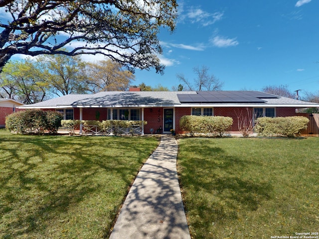 ranch-style home with a chimney, brick siding, solar panels, and a front lawn