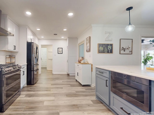 kitchen featuring white cabinetry, crown molding, wall chimney range hood, and appliances with stainless steel finishes