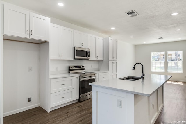 kitchen with dark wood-style floors, a center island with sink, a sink, white cabinets, and appliances with stainless steel finishes