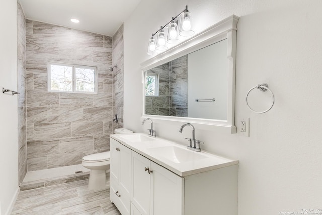 bathroom with double vanity, toilet, tiled shower, and a sink