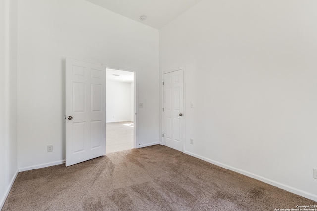 carpeted empty room featuring baseboards and a towering ceiling