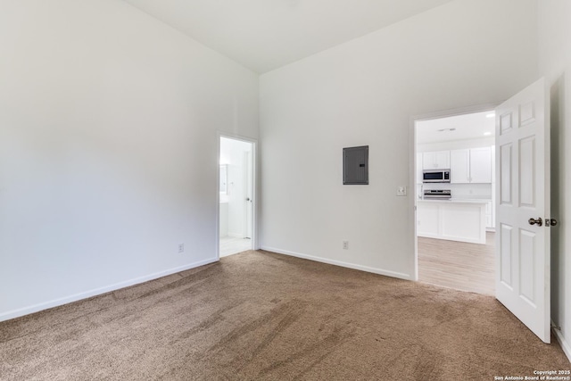 empty room with electric panel, baseboards, light carpet, and a towering ceiling