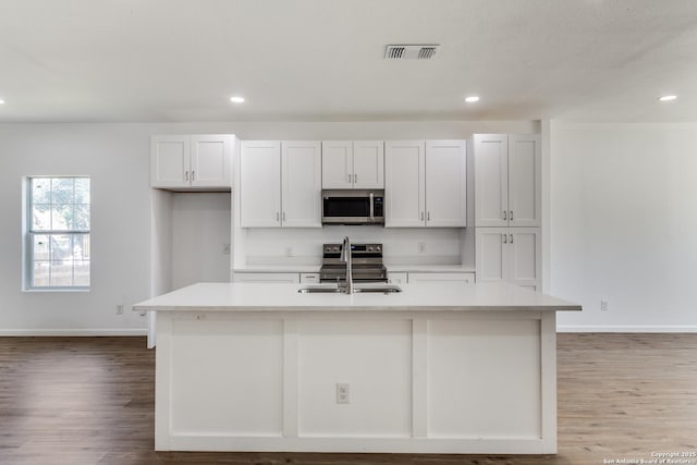 kitchen with visible vents, a center island with sink, appliances with stainless steel finishes, and light countertops