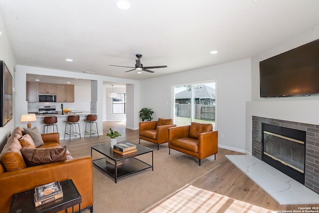 living area featuring recessed lighting, light wood-style floors, baseboards, a brick fireplace, and ceiling fan