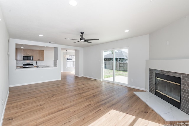 unfurnished living room featuring light wood finished floors, a fireplace, baseboards, and a ceiling fan