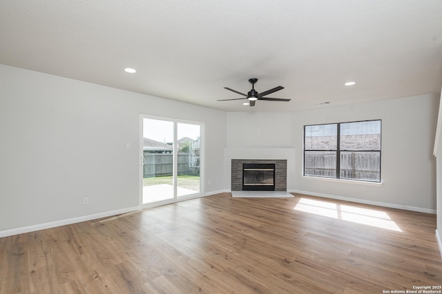 unfurnished living room with visible vents, wood finished floors, a fireplace, baseboards, and ceiling fan