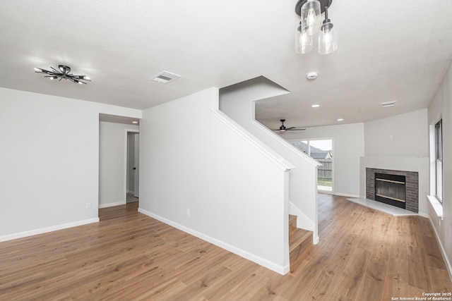 unfurnished living room featuring visible vents, a brick fireplace, baseboards, stairs, and light wood-style flooring