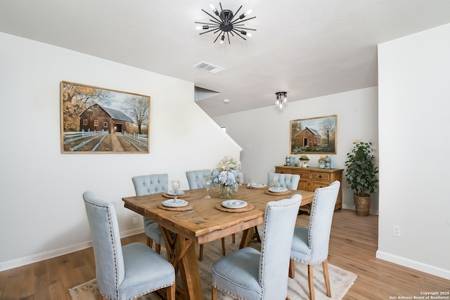 dining area with visible vents, light wood-style flooring, baseboards, and an inviting chandelier