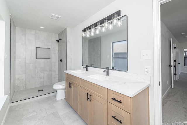 bathroom featuring toilet, visible vents, a tile shower, and a sink