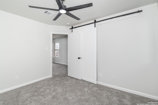 empty room with a ceiling fan, visible vents, baseboards, a barn door, and carpet flooring