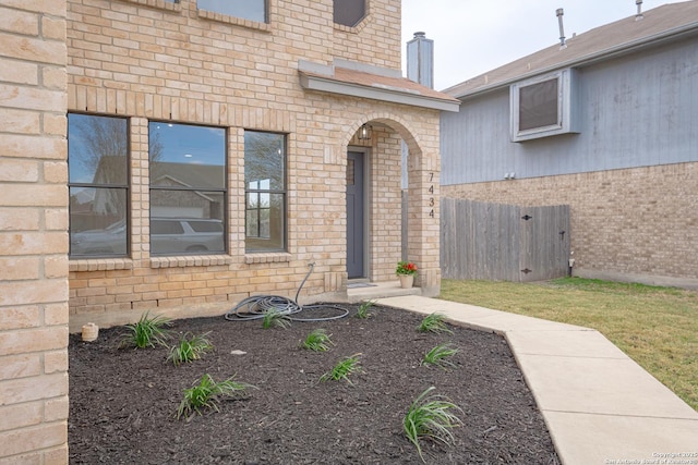 view of exterior entry featuring brick siding and fence