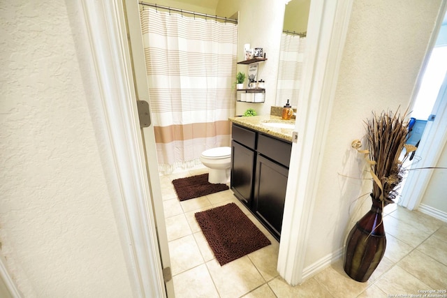 bathroom with vanity, baseboards, tile patterned floors, toilet, and a textured wall