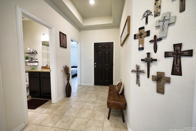 entryway with light tile patterned flooring, a tray ceiling, and baseboards