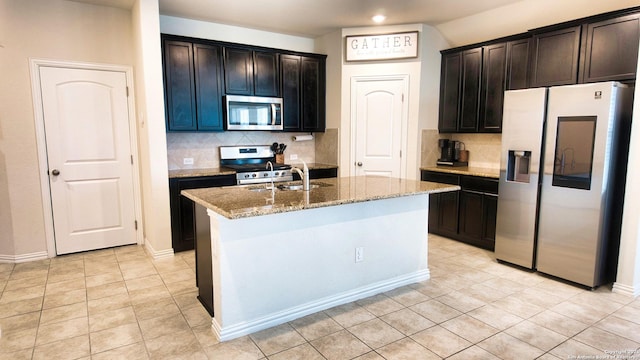 kitchen with an island with sink, a sink, backsplash, appliances with stainless steel finishes, and light stone countertops