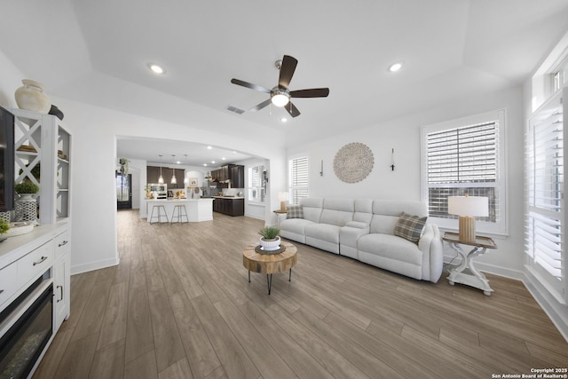 living area featuring a ceiling fan, wood finished floors, visible vents, a tray ceiling, and recessed lighting