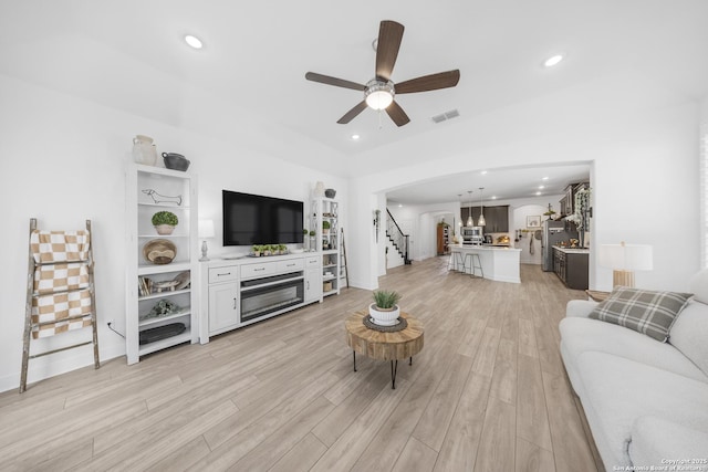 living room featuring visible vents, a ceiling fan, stairway, arched walkways, and light wood-style floors