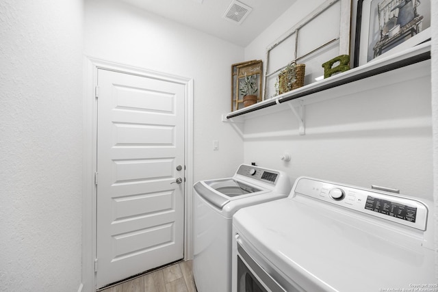 washroom with washing machine and clothes dryer, laundry area, light wood-style flooring, and visible vents