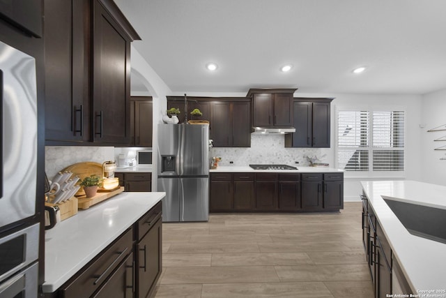 kitchen with under cabinet range hood, light countertops, decorative backsplash, stainless steel fridge, and gas stovetop