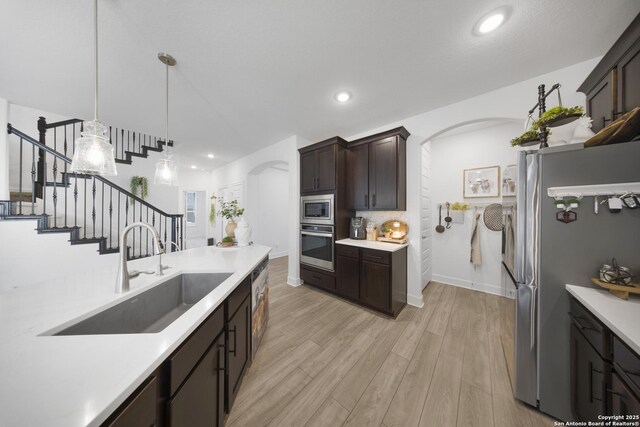 kitchen featuring a sink, stainless steel appliances, arched walkways, dark brown cabinetry, and light countertops