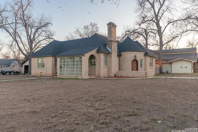 french country inspired facade with a shingled roof, brick siding, and a chimney