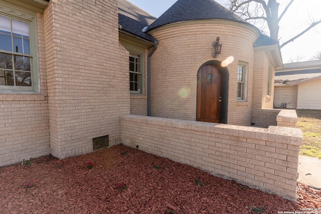 doorway to property with brick siding and a shingled roof