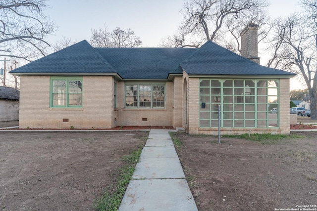 view of front facade featuring roof with shingles, a sunroom, crawl space, brick siding, and a chimney