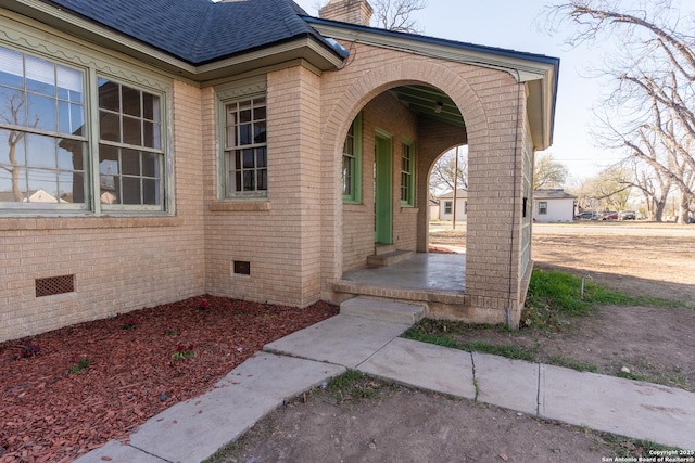 doorway to property with crawl space, brick siding, roof with shingles, and a chimney