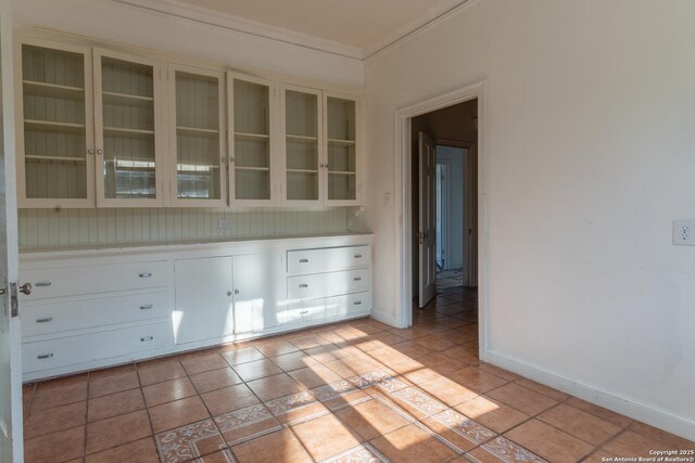 interior space with light countertops, light tile patterned floors, glass insert cabinets, and ornamental molding